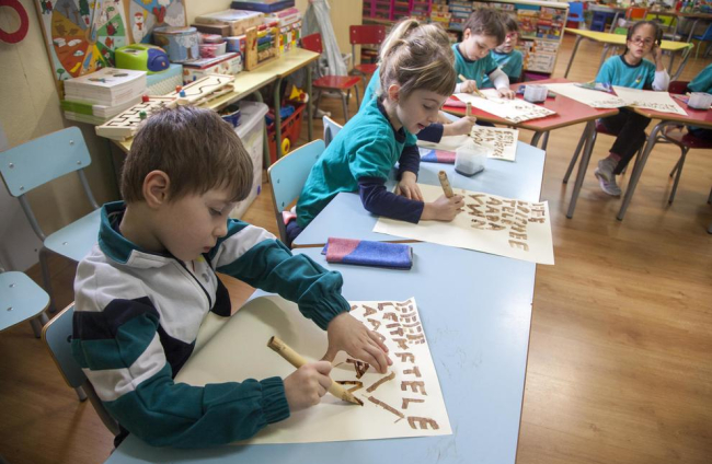 Los escolares muestran letras mayúsculas que escribieron con cañas y tinta. 