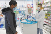 Imagen de un empleado de una farmacia de Lleida mostrando las mascarillas que venden a un cliente.