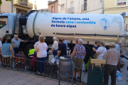 Vecinos de Bovera hacían cola el viernes para llenar sus garrafas ante una cuba con un eslógan a favor de beber agua del grifo.