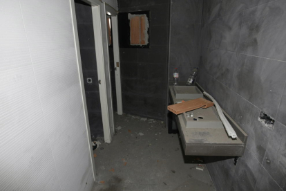 L’interior de dos estances de l’edifici, completament desvalisades, amb l’ascensor trencat, cables penjant i un lavabo sense aixetes.