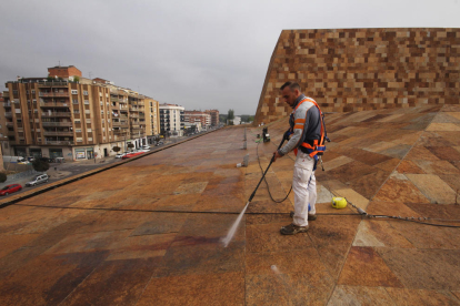Un operari a la coberta de l’edifici netejant la pedra amb aigua a pressió.