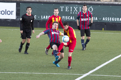 Dos jugadores pugnan por el control del balón en presencia del árbitro del partido y otros futbolistas.