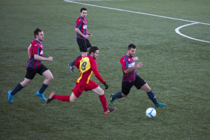 Dos jugadores pugnan por el control del balón en presencia del árbitro del partido y otros futbolistas.