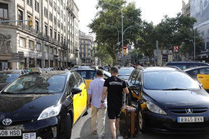 Varios turistas pasan entre los taxis que ocupan la Gran Vía de Barcelona.