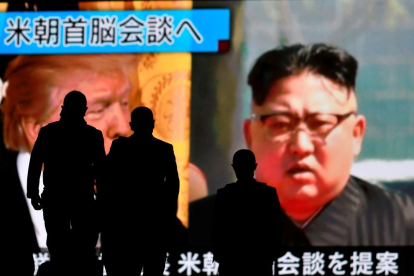Personas pasan por delante de una pantalla con la imagen de los líderes de EEUU y Corea del Norte.