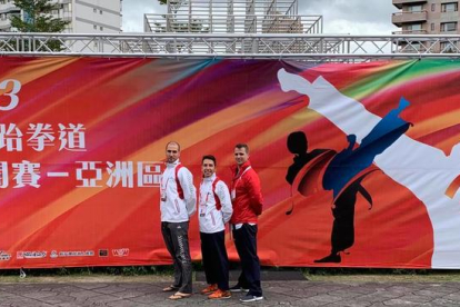 Els tres integrants de la selecció espanyola de taekwondo posen al costat d’un dels cartells que anuncien el Mundial a Taipei.