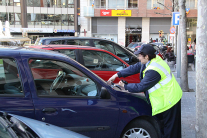 Una vigilant de zona blava imposa una multa a un vehicle.