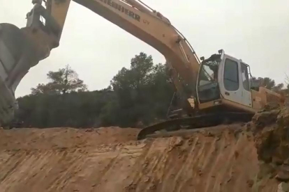 Una máquina trabajando al lado de un muro de piedra seca.