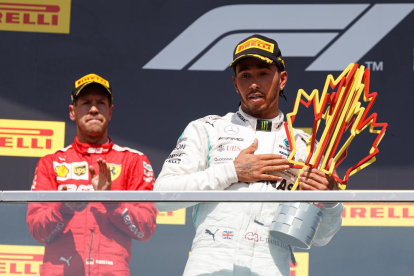 Hamilton, en el podio con el trofeo de ganador, y Vettel, detrás, resignado tras la sanción. 