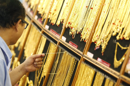 Un hombre sostiene collares de oro en un local de venta de oro. 