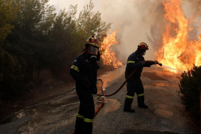 Varios bomberos tratan de extinguir un incendio en Penteli, al norte de la capital de Grecia.