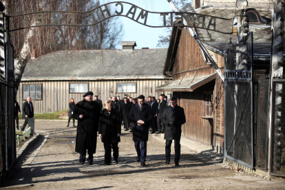 Merkel cruza la entrada del campo de concentración de Auschwitz, bajo el siniestro cartel “El trabajo os hará libres”.