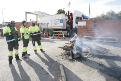 Un camión cruzado bloquea la entrada del vertedero comarcal y empleados del servicio de recogida se calientan ante un fuego. 