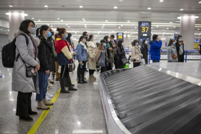 Pasajeros (con mascarilla) esperan para recoger su equipaje en el aeropuerto de Shanghái. 