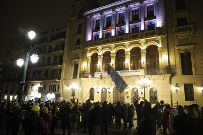 Los concentrados observan cómo tres encapuchados arrían la bandera española de uno de los mástiles del balcón de la Paeria.