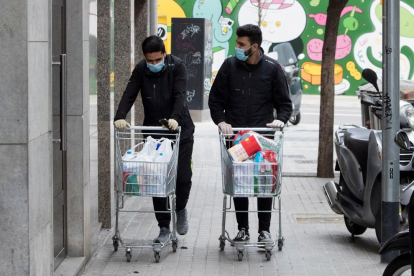 Dos treballadors d’un supermercat de Barcelona porten la compra a casa d’uns clients.
