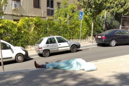 Imatge d'un home dormint a ple sol al barri.