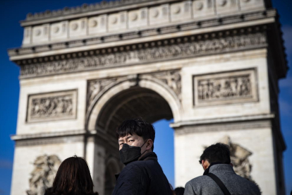 Diversos turistes passegen davant l’Arc del Triomf de París.
