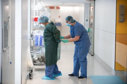 Una profesional sanitaria ata a una compañera una bata antes de atender a un paciente con covid-19, en uno de los bloques quirúrgicos del Hospital Clínic de Barcelona habilitado como UCI.