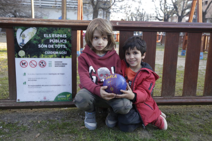 Dos niños pequeños con una pelota ayer en una plaza de Balàfia ante un cartel con la prohibición.