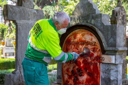 Un operario limpia la lápida manchada con pintura roja.