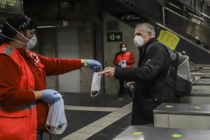 Una voluntària de la Creu Roja entrega una mascareta a un passatger, ahir, en una estació de la xarxa de metro de Barcelona.