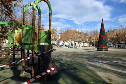 La plaça del Planell de Linyola, amb una instal·lació infantil precintada i un gran arbre de Nadal.