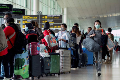 Varios viajeros en el aeropuerto de Barcelona, muchos de ellos con mascarillas.