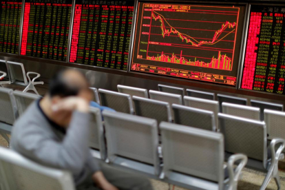Un hombre descansa frente al panel que muestra la evolución de la bolsa de Shanghái, en China.