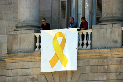 Tres operaris col·loquen de nou el llaç groc a la façana de l’ajuntament de Barcelona.