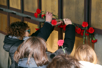 Familiares depositando claveles rojos bajo las placas que recuerdan a las víctimas de la Guerra Civil.