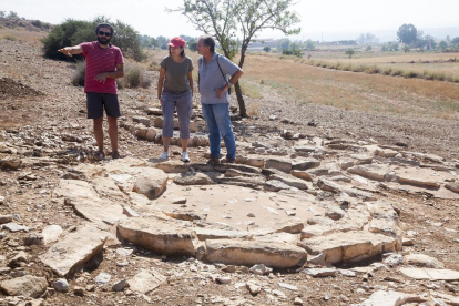 Un responsable de la excavación mostrando los túmulos de la necrópolis a unos visitantes. 