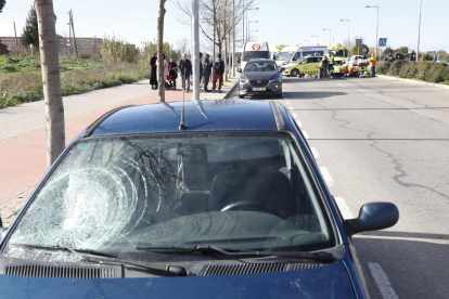 Vista del vehículo, con el impacto en el parabrisas,  y al fondo, la atención de los servicios de emergencias a la viandante herida. 