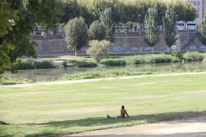 Un jove a l'ombra en una imatge d'arxiu a la canalització del riu a Lleida.