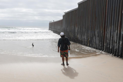Un hombre parado frente al muro construido en la frontera sur de Estados Unidos.