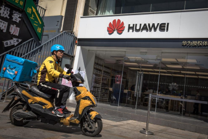 Un repartidor en motocicleta davant una botiga de Huawei, ahir dilluns a Pequín.