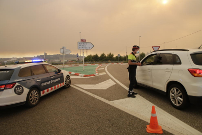 Mossos d’Esquadra se protegían ayer de las cenizas con máscaras para informar a los conductores del corte de la carretera C-12 en Maials.