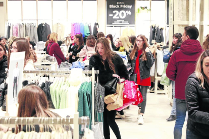 Numerosas personas en una tienda de ropa, con una joven con varias bolsas.