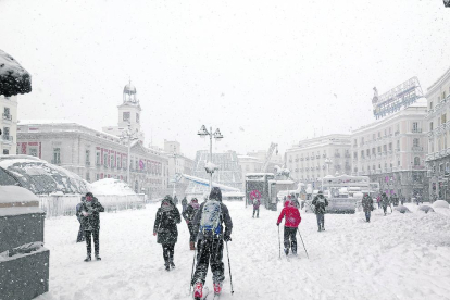 Varias personas caminan por la Puerta del Sol cubierta de nieve.