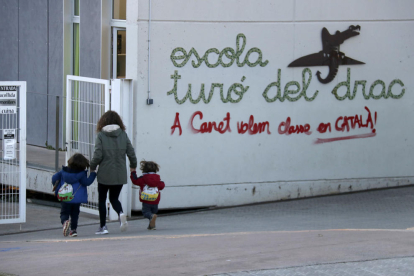 Una madre acompaña a sus hijos a la escuela Turó del Drac de Canet de Mar. Una pintada reclama la enseñanza en catalán en la fachada del centro.