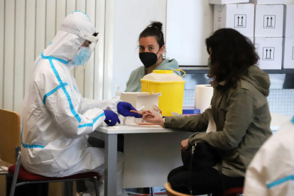 A l’esquerra, un sanitari fa una prova serològica a un alumne per saber si té anticossos del virus i a la dreta, una estudiant es fa la PCR ella mateixa.