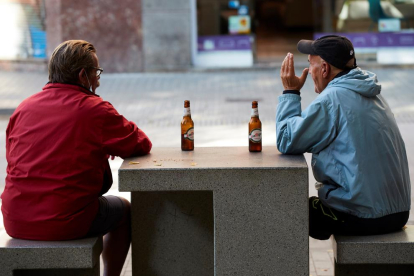 Diverses persones prenen una cervesa en un banc d'un carrer del centre de Barcelona.