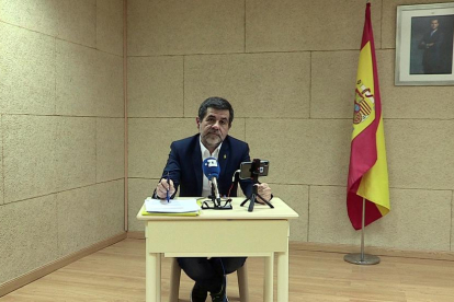 Jordi Sànchez tuvo que comparecer junto a una bandera española y una imagen del rey, sentado en una mesita con apenas sitio.