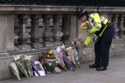 Una policia britànica diposita flors a prop del Parlament al costat d’un retrat de l’agent assassinat.