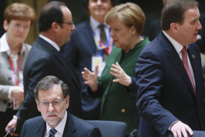 Rajoy sentado mientras Merkel y Hollande charlan antes del inicio de la cumbre.
