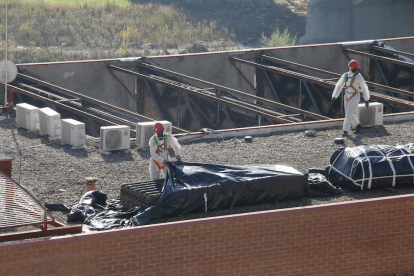 Operarios con trajes de protección cubren el amianto retirado de la cubierta del edificio de Mercolleida.