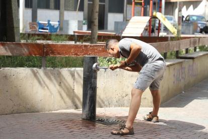 Un home es refresca en una font a Lleida.