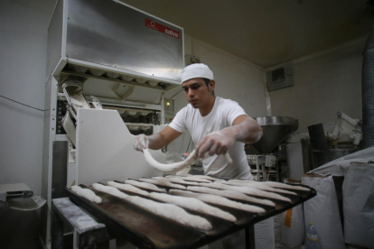 Un trabajador prepara barras de pan en el obrador.