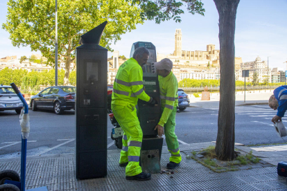 Dos operarios municipales retiran un parquímetro de Eysa, que está al lado de uno nuevo de la EMAU. 