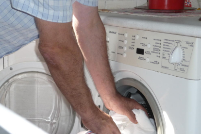 Un hombre introduce ropa en una lavadora doméstica.